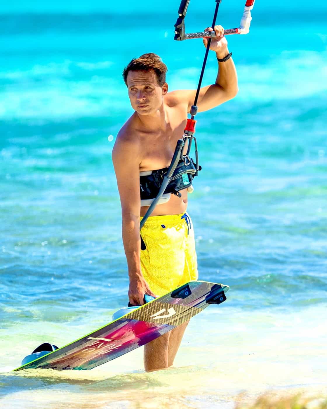 Jeremie Tronet holding a kiteboard in shallow turquoise water
